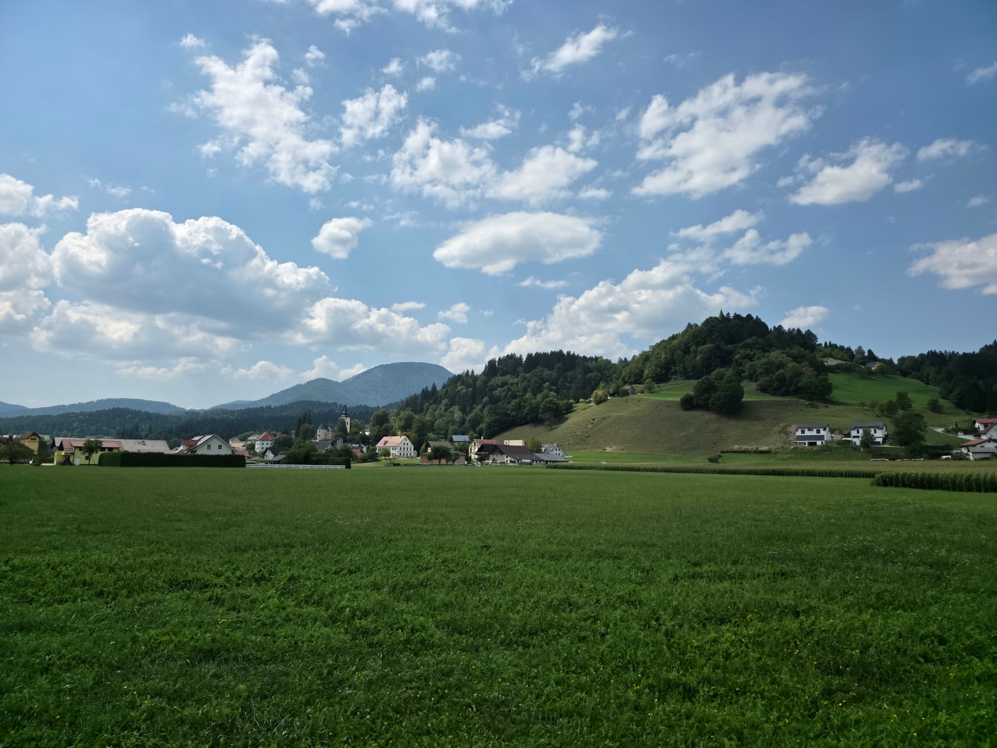 Zelena gričevnata pokrajina z vasjo pod modrim nebom